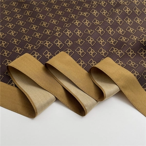 Dettaglio di un foulard in seta con monogramma DXG dorato e bordo giallo acceso
