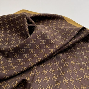 Dettaglio macro di sciarpa in seta con motivo monogramma marrone oro e trama twill