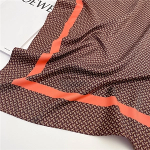 Detailed close-up of silk-textured square scarf with monogram pattern and orange border