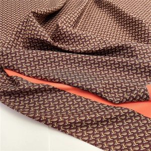 Macro view of monogram pattern textile with vibrant orange lining and smooth silk texture