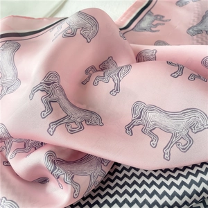 Dettaglio di sciarpa in seta rosa con stampa astratta di cavalli e trama liscia