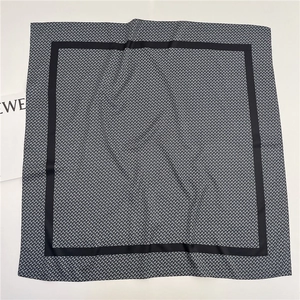 Macro detail of silk scarf showing grey anagram pattern and black border edges