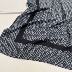 Macro detail of silk scarf featuring letter logo print and contrast black border edges