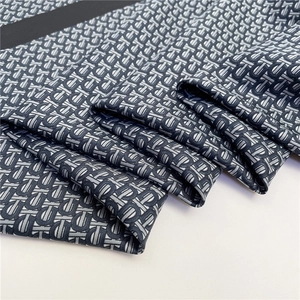 Close-up of luxury silk scarf showing intricate TB monogram pattern in deep blue and grey