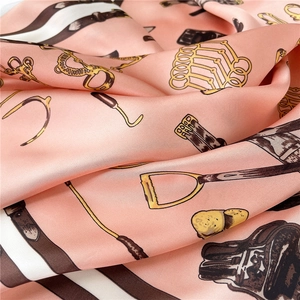 Detailed close-up of pink silk square scarf featuring golden equestrian horse bit patterns