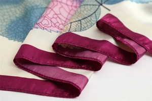 Detailed view of leaf pattern silk scarf with magenta satin edges and smooth texture