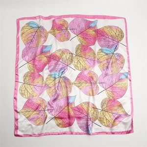 Detailed view of colorful leaf patterns on a soft beige silk scarf with pink edges