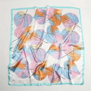 Close-up of lightweight square silk scarf with vibrant gradient leaf patterns and blue hem