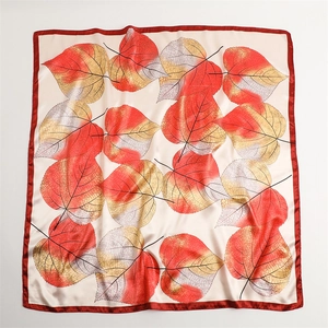 Flat lay of square silk scarf featuring red borders and vibrant leaf prints on cream satin