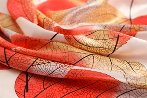 Detailed close-up of vibrant red and orange maple leaf patterns on soft silk scarf fabric