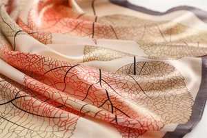 Close-up of elegant leaf vein pattern on silky beige satin scarf with rolled edges