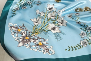 Detailed close-up of light blue floral satin scarf with elegant lily flower print and green border