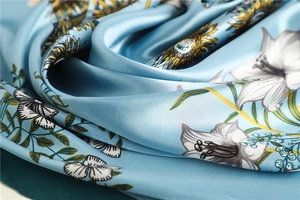 Macro detail of sky blue satin scarf showing sunflower and butterfly print texture