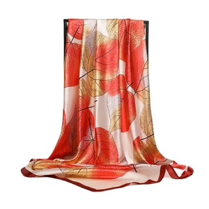 Elegant silk-like scarf with autumn maple leaf pattern hanging on a minimalist stand