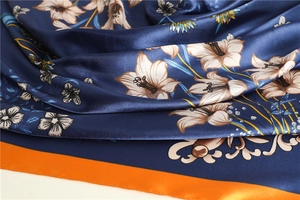 Detailed close-up of navy and orange silk scarf featuring elegant white lily patterns