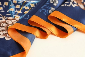 Close-up of floral satin silk square scarf with orange borders and navy blue petal print