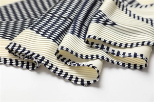 Macro detail of pleated geometric silk scarf with black and white checkered pattern borders