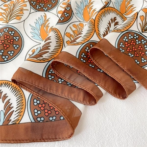 Détail d'un foulard en soie aux motifs de feuilles orange et bleu avec bordure marron