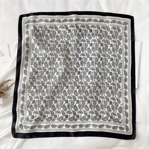 Détail d'un foulard en soie à motif cachemire avec bordure noire sur fond minimaliste