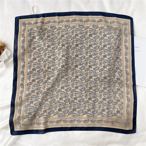 Détail du foulard en soie à motif paisley, bordure bleue et fond couleur champagne