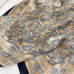 Détail de la texture du foulard en soie paisley avec finition satinée dorée et bord bleu