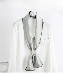 Détail d'un foulard en soie vert-gris à rayures noué sur une chemise blanche