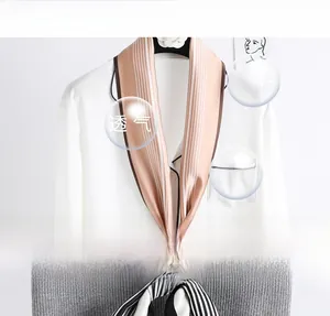 Détail d'un foulard en soie à rayures champagne sur un chemisier blanc et un sac