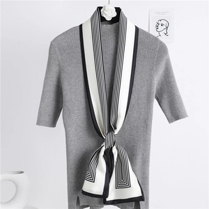 Détail d'un foulard fin à rayures noires et blanches avec un haut en maille grise