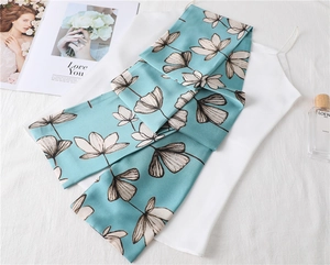 Close-up of a teal floral silk scarf draped over a white satin top with a perfume bottle
