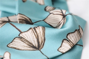 Macro detail of elegant blue silk scarf featuring ivory ginkgo leaf patterns and texture