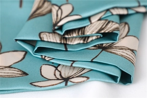 Macro shot of elegant turquoise silk scarf with white magnolia floral print texture