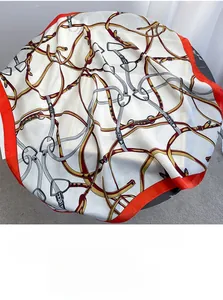 Close-up of square silk scarf featuring classic golden chain and horsebit prints with red borders