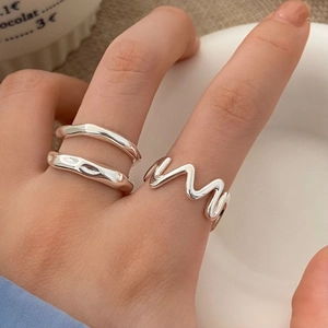 Detail of irregular silver textured rings worn on fingers with a minimalist aesthetic