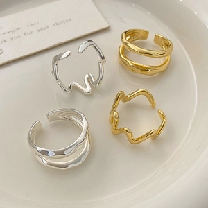 Close-up of irregular wavy open rings in gold and silver finish on a ceramic tray