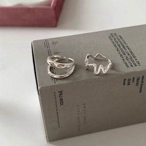 Close-up of dual silver irregular wavy open rings on a minimalist textured surface