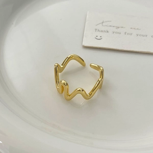 Close-up of irregular wave gold open ring with polished finish on white ceramic tray