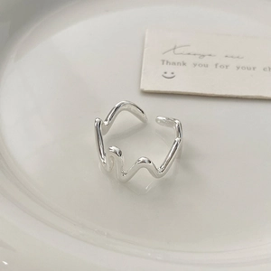 Detailed close-up of a minimalist silver wavy irregular ring on a white ceramic tray