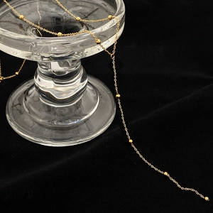 Détail d'un collier chaîne dorée à billes délicates sur fond de velours noir