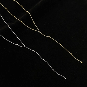 Détail de colliers perlés minimalistes en forme de Y en or et argent sur velours noir