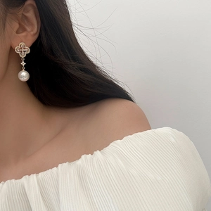 Close-up of pearl drop earrings with clover zircon stud worn by a model in soft light