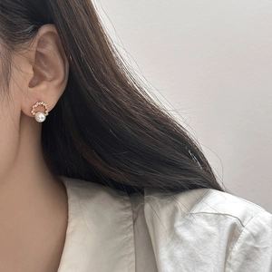 Close-up of elegant pearl earrings with gold base and sparkling zircon accents on a model