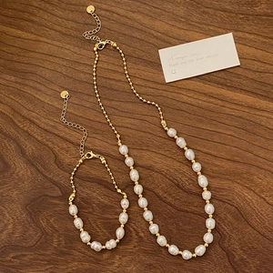 Detail of freshwater pearl necklace and bracelet set with gold beads on dark wood surface