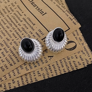 Macro shot of retro silver geometric earrings with oval black stone on vintage newspaper
