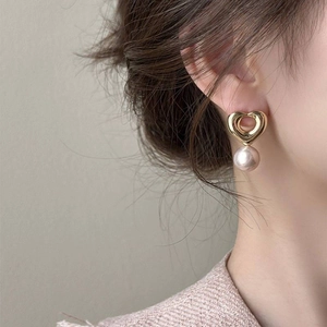 Détail d'une boucle d'oreille cœur vintage dorée avec une perle rose champagne ronde