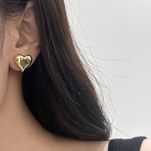 Close-up of a polished golden heart-shaped stud earring worn on a female ear