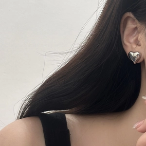 Close-up of a glossy silver heart stud earring worn on ear with polished finish