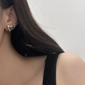 Close-up of a glossy silver heart-shaped stud earring worn on a model's earlobe