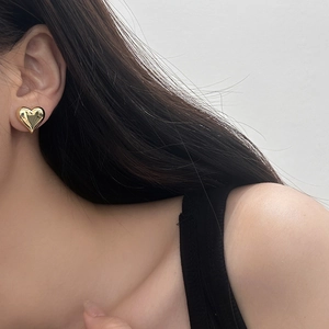 Close-up of a polished golden 3D heart stud earring worn on ear, showing sleek metallic texture