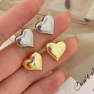 Close-up of minimalist heart stud earrings in polished gold and silver metal finishes