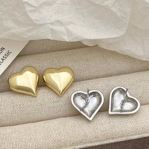 Polished heart-shaped stud earrings in gold and silver finish on a textured jewelry tray
